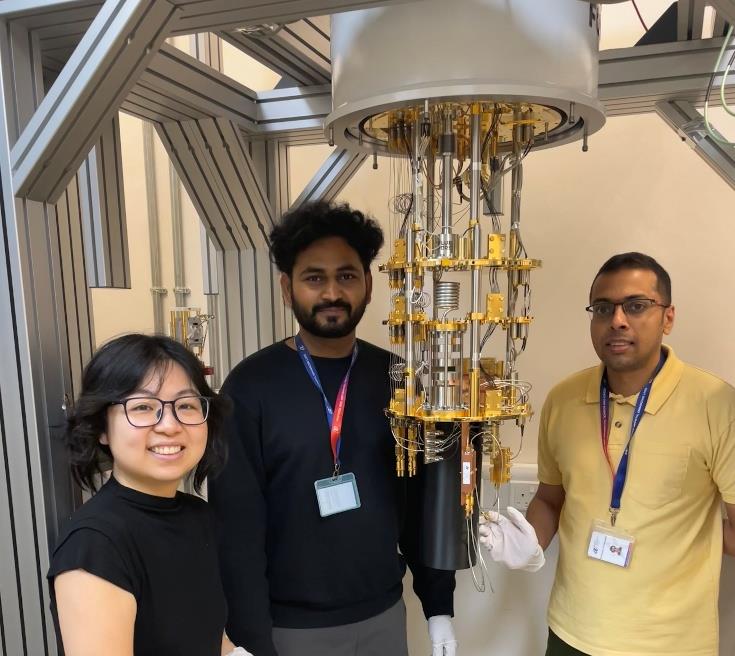 Three people standing next to a dilution refrigerator in the NQFF lab in Singapore